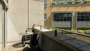 A balcony with a table and chairs, a concrete wall, and a building with windows and plants. - Cove St Martin’s (London)