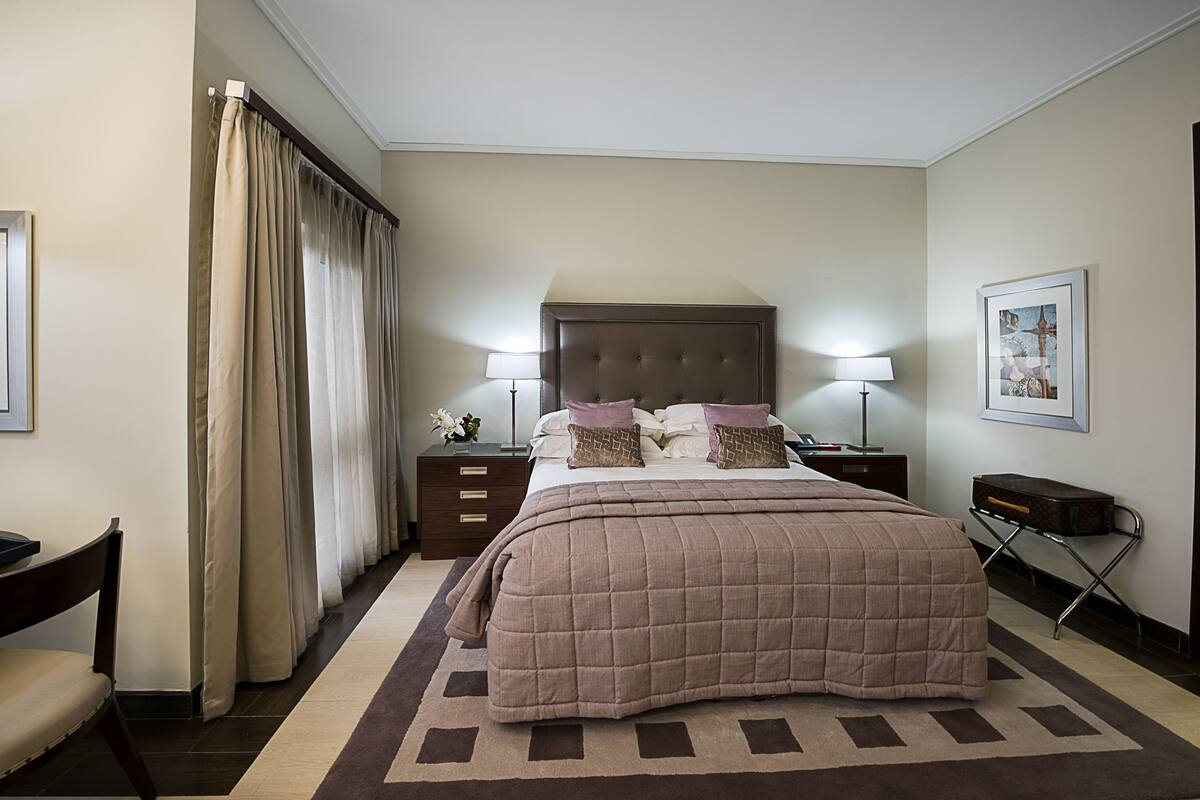 A neatly arranged bedroom with a large bed, bedside tables, a chair, and a lamp.