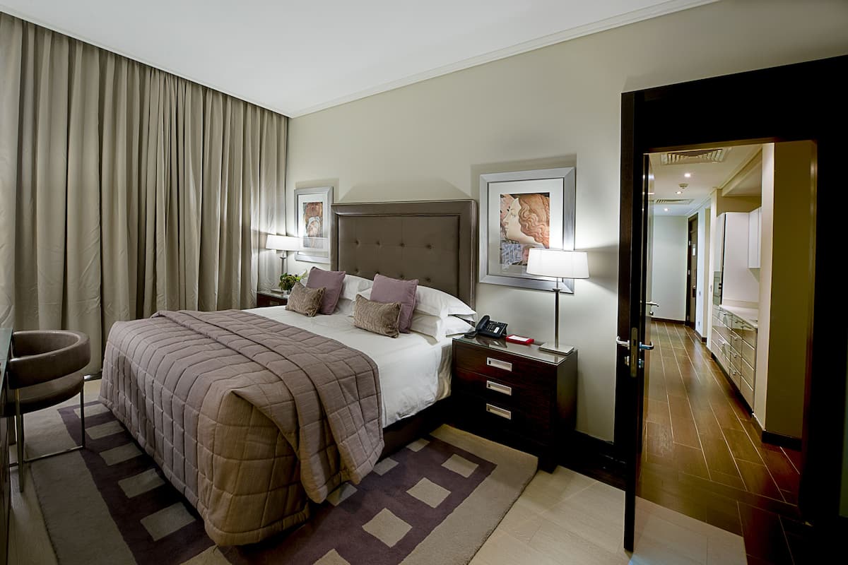 A hotel room with a large bed, bedside tables, a chair, and a door leading to a bathroom.