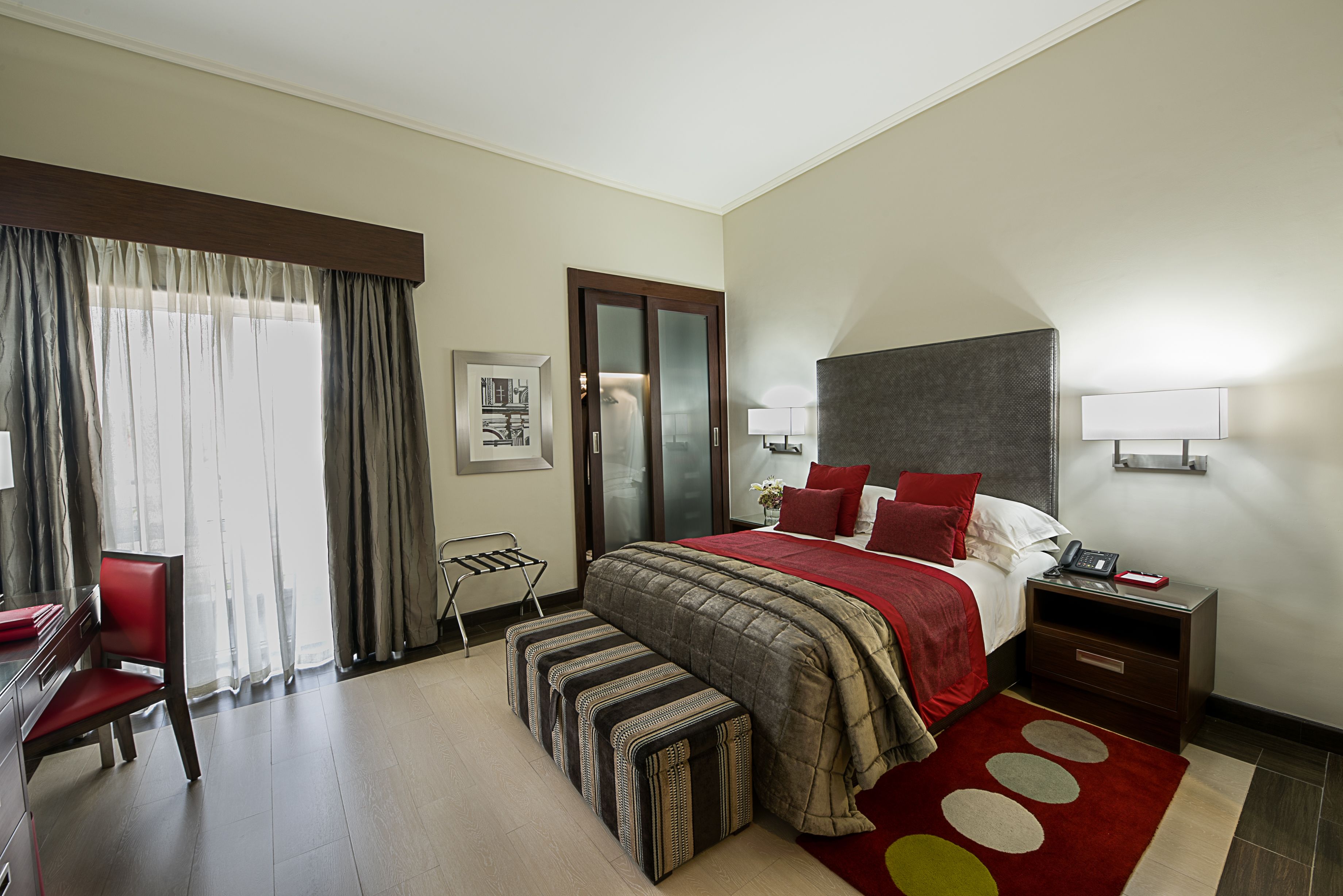 A hotel room with a large bed, a desk, a chair, and a window with curtains.