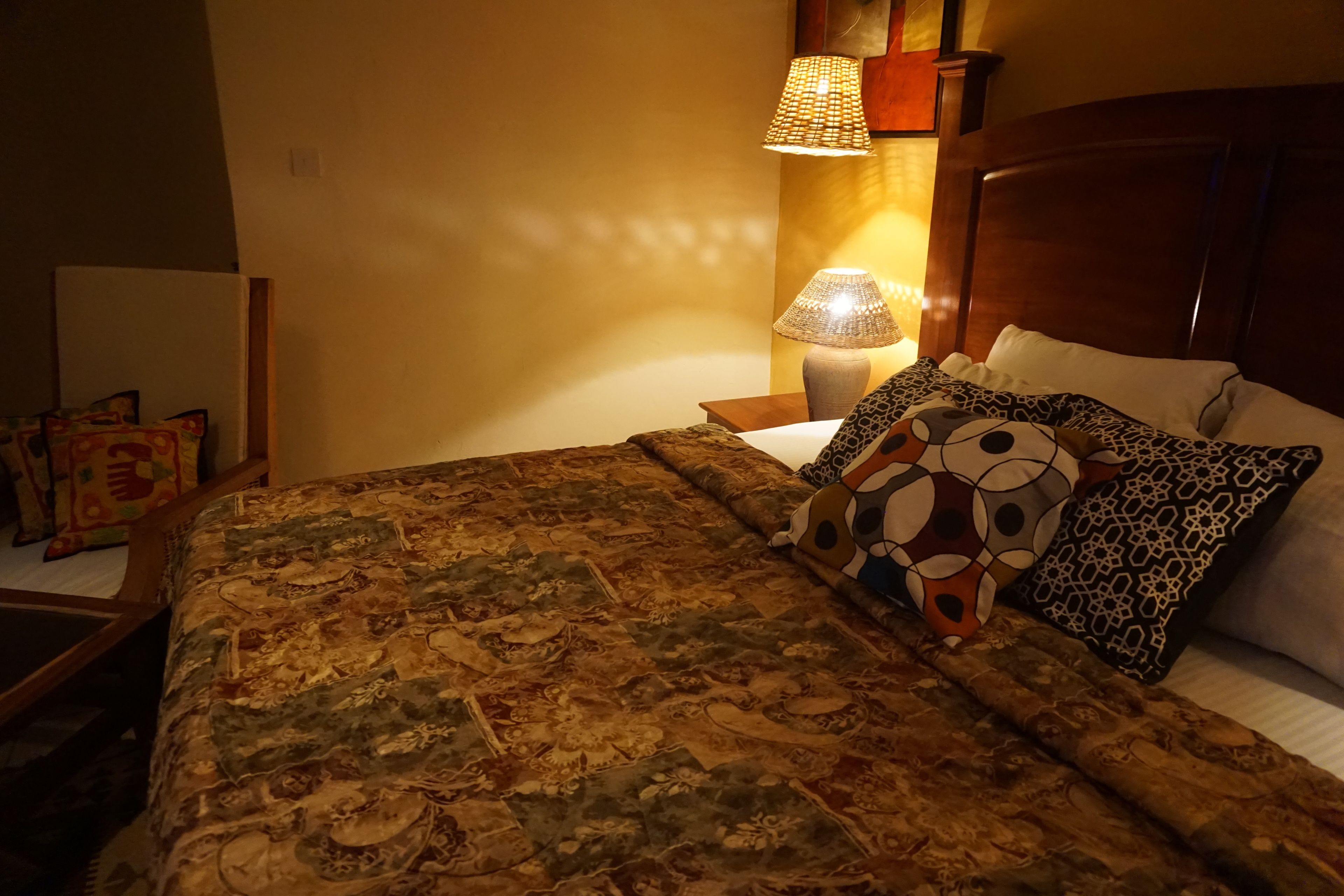 A neatly made bed with a patterned bedspread, a wooden headboard, and multiple decorative pillows.
