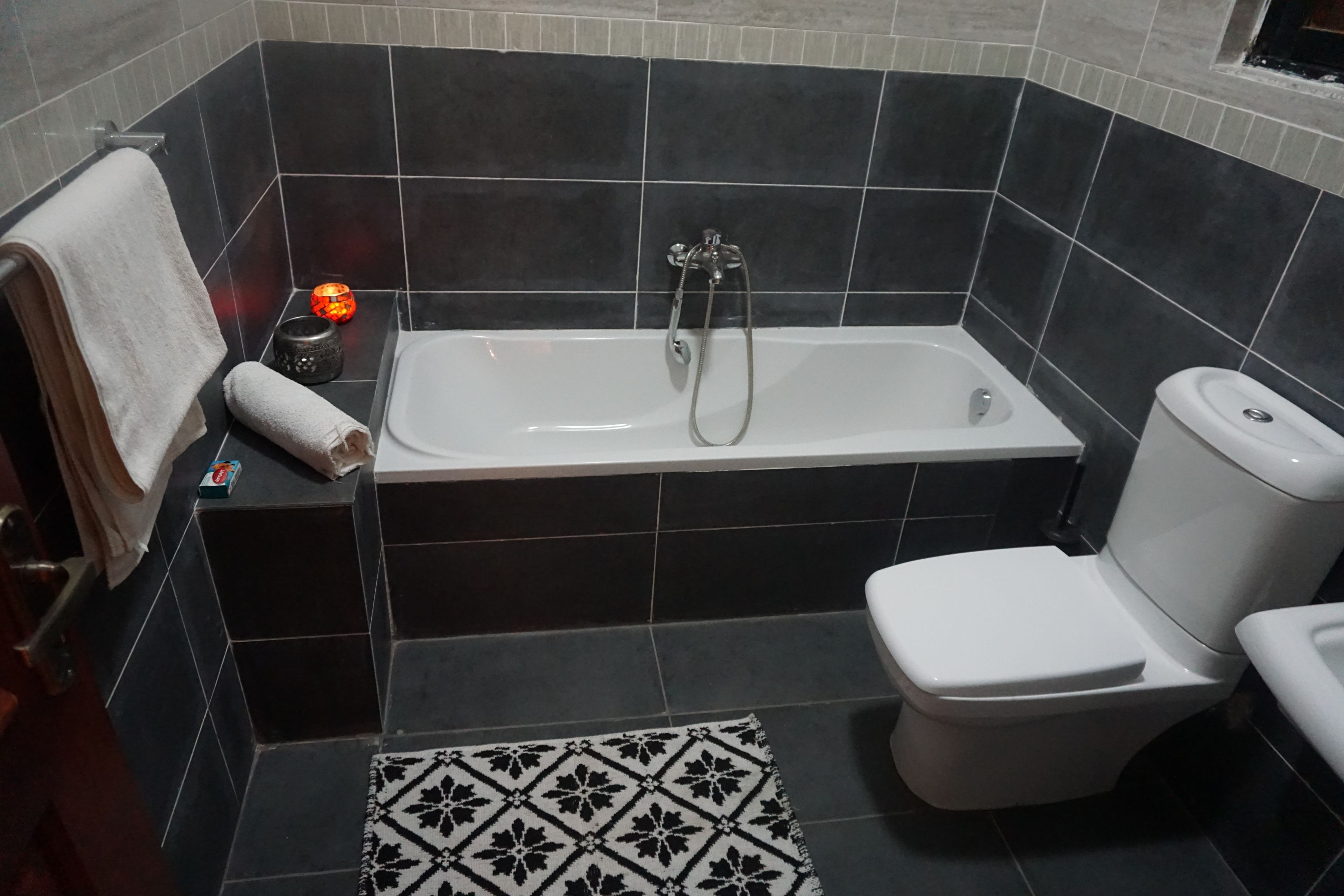 A bathroom with a bathtub, toilet, and a patterned rug.