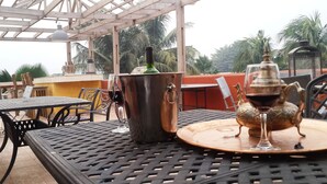 An outdoor dining area with a metal table and chairs, a copper pot, and a glass with a decorative base. - Accra Royal Castle Apartments & Suites (Kwabenya)