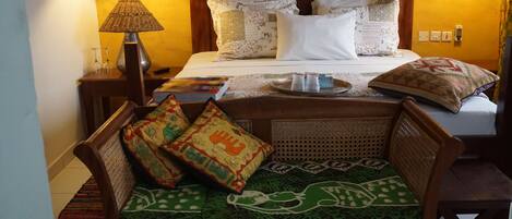 Ein Hotelzimmer mit Bett, einer Holzbank mit Kissen, einer Lampe und einem Tablett mit Flasche und Gläsern.