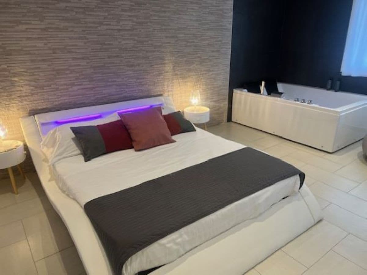 A modern bedroom with a large bed, bedside lamps, and a built-in bathtub.