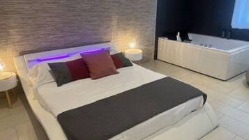 A modern bedroom with a large bed, bedside lamps, and a built-in bathtub.
