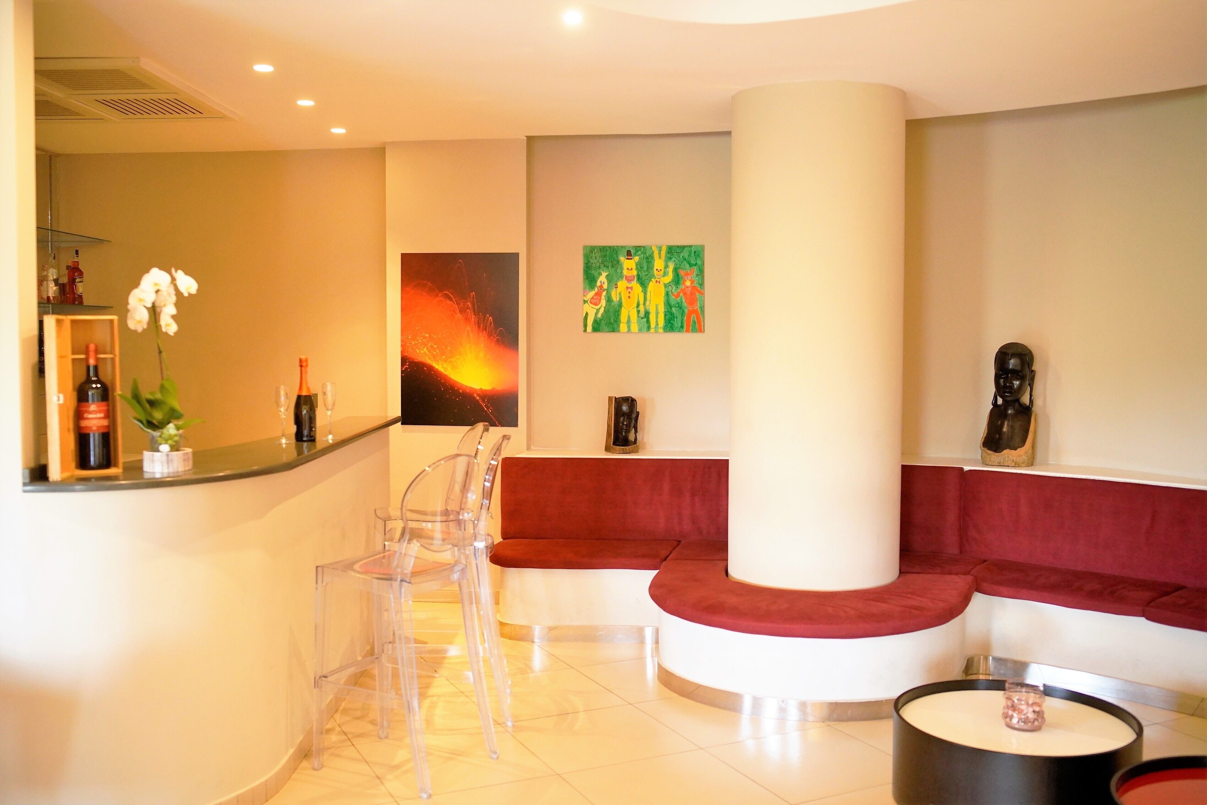 Un vestíbulo moderno con una zona de estar curva color rojo, un mostrador de recepción con sillas transparentes y una columna grande.