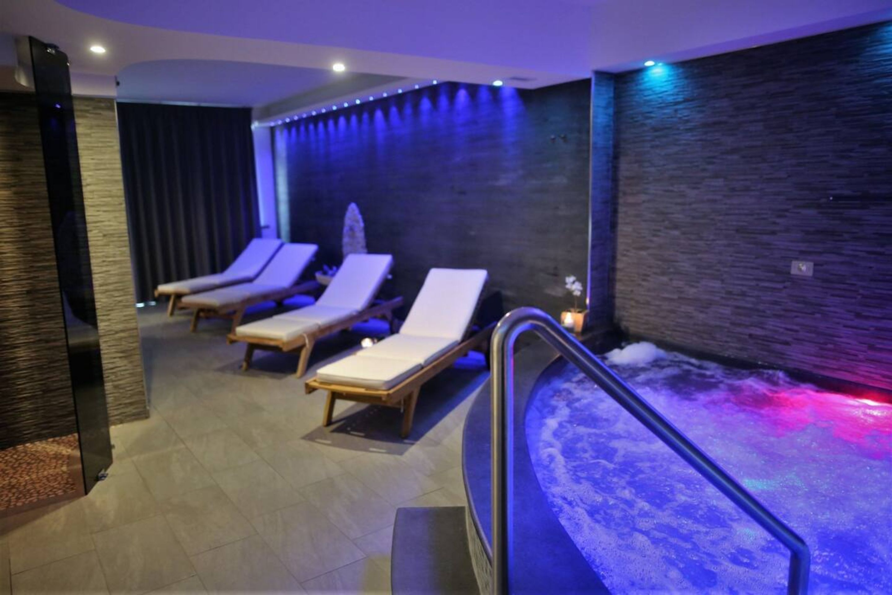 A spa area with three sun loungers, a hot tub, and a textured wall.