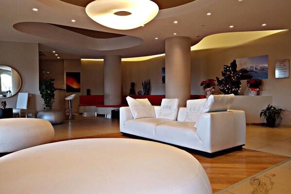 A spacious lobby with a white sofa, a large mirror, and a red accent wall. - Mareneve Resort (Linguaglossa)