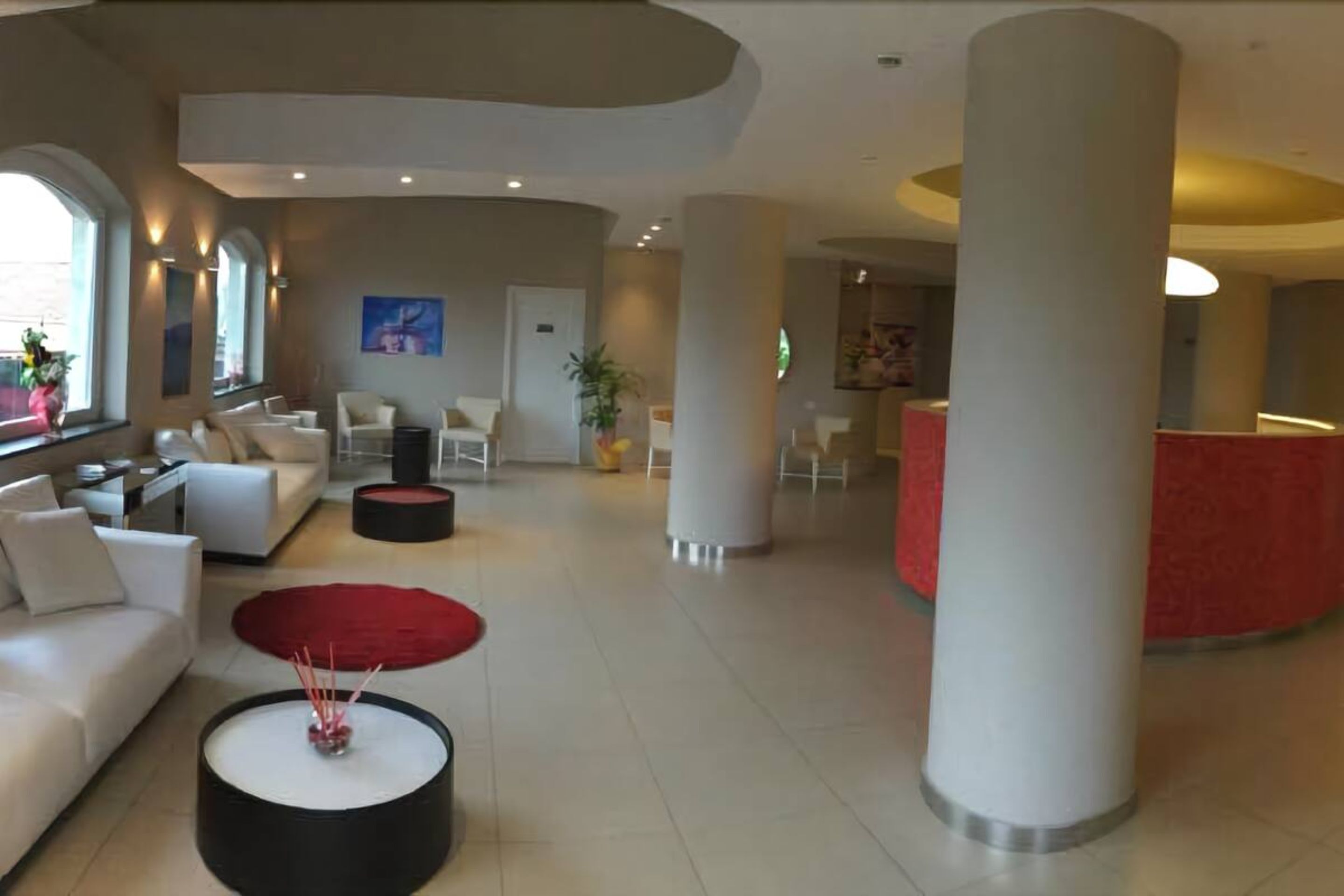 Een ruime lobby met een modern ontwerp, met een witte bank, een ronde rode tafel en een receptiebalie met een rode accentmuur.
