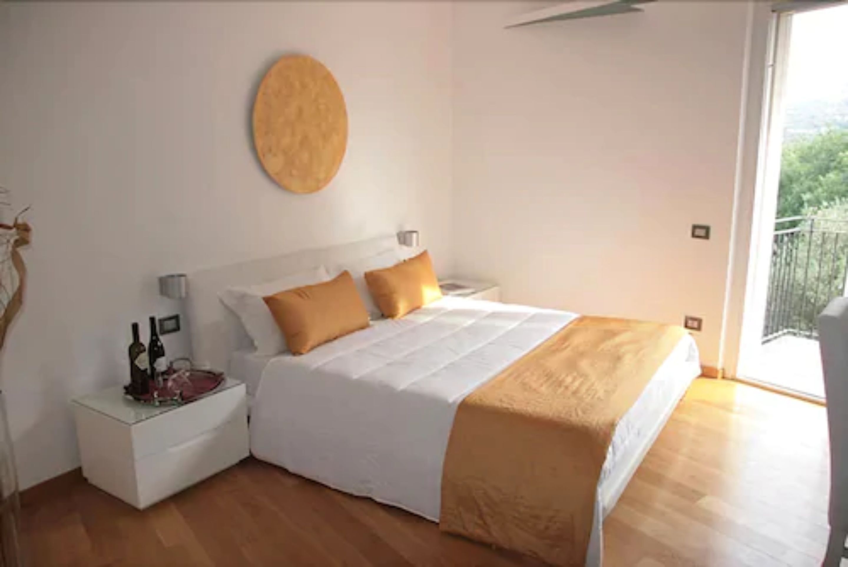 A bedroom with a bed, a nightstand, a round wall decoration, and a balcony view.