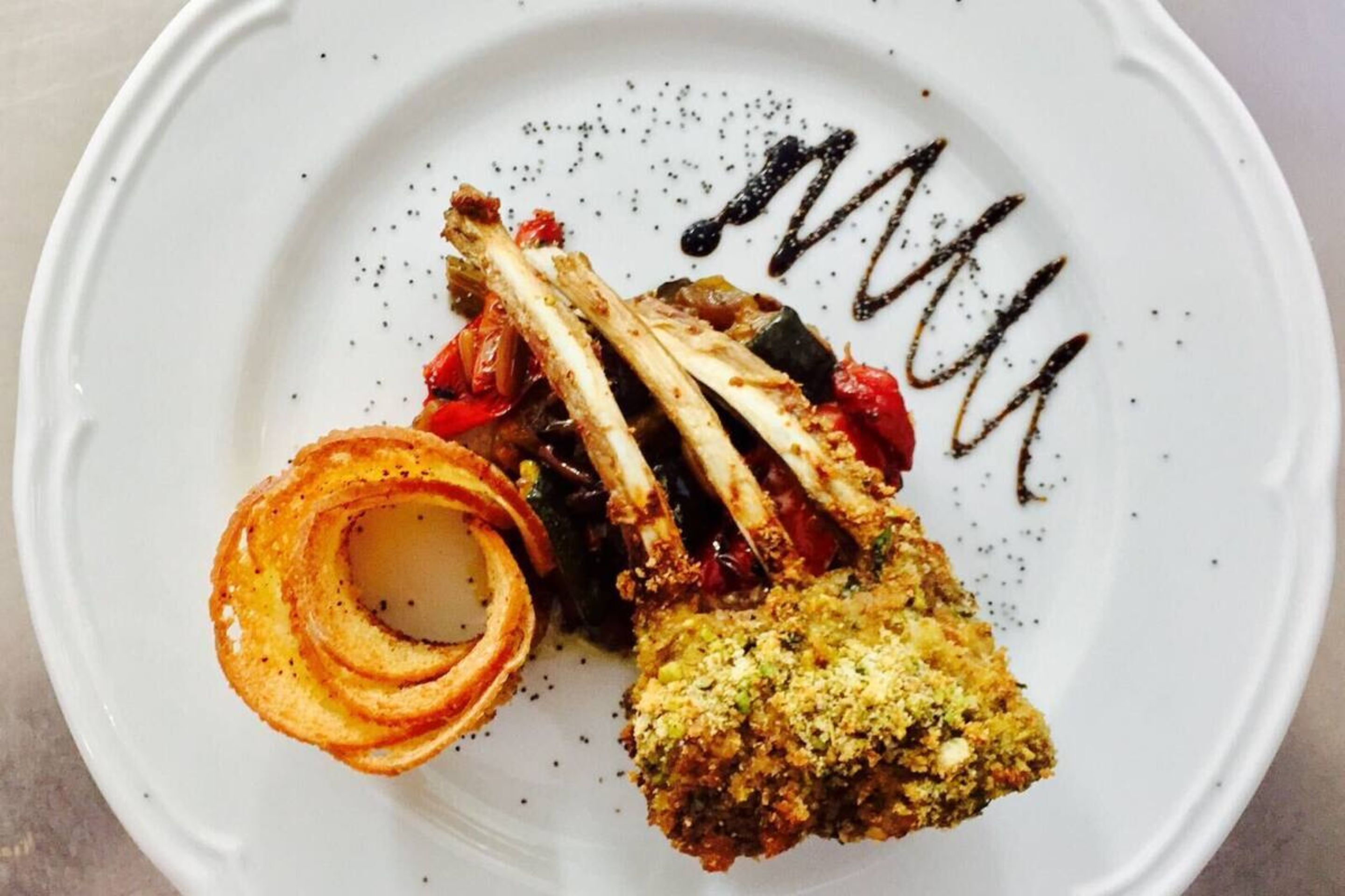 A plate with a lamb chop, a breaded item, and a spiral of what appears to be onion rings.