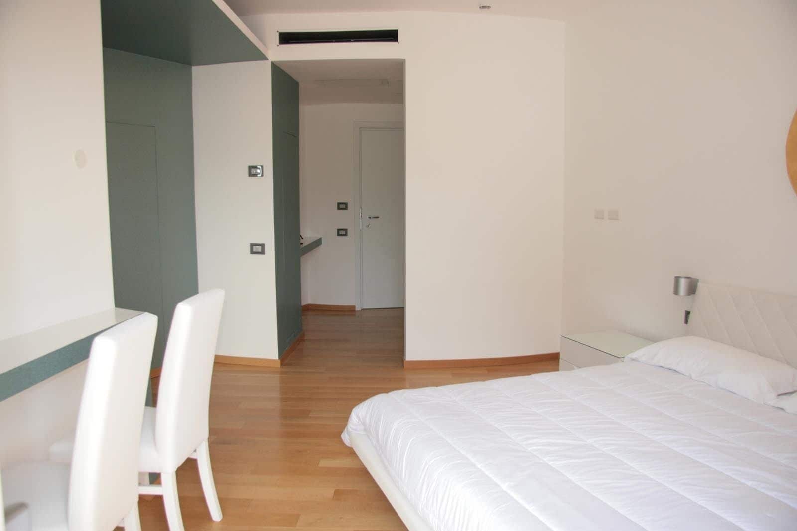 Una camera da letto con un letto, una scrivania e sedie, e una porta che dà su un'altra stanza.
