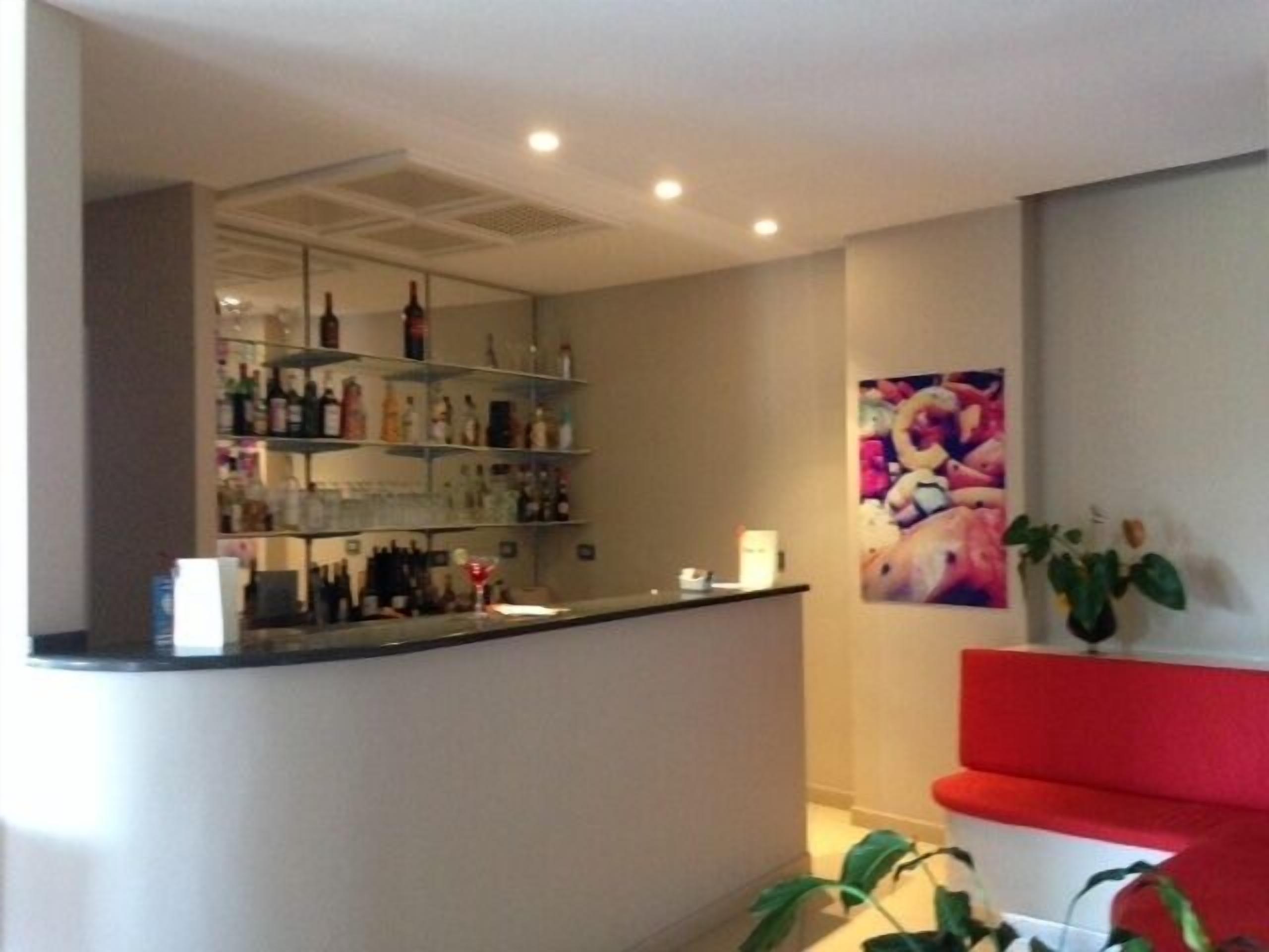 Eine Bar mit Regalen voller Flaschen, einem roten Sofa und einer Wand mit einem farbenfrohen Gemälde.