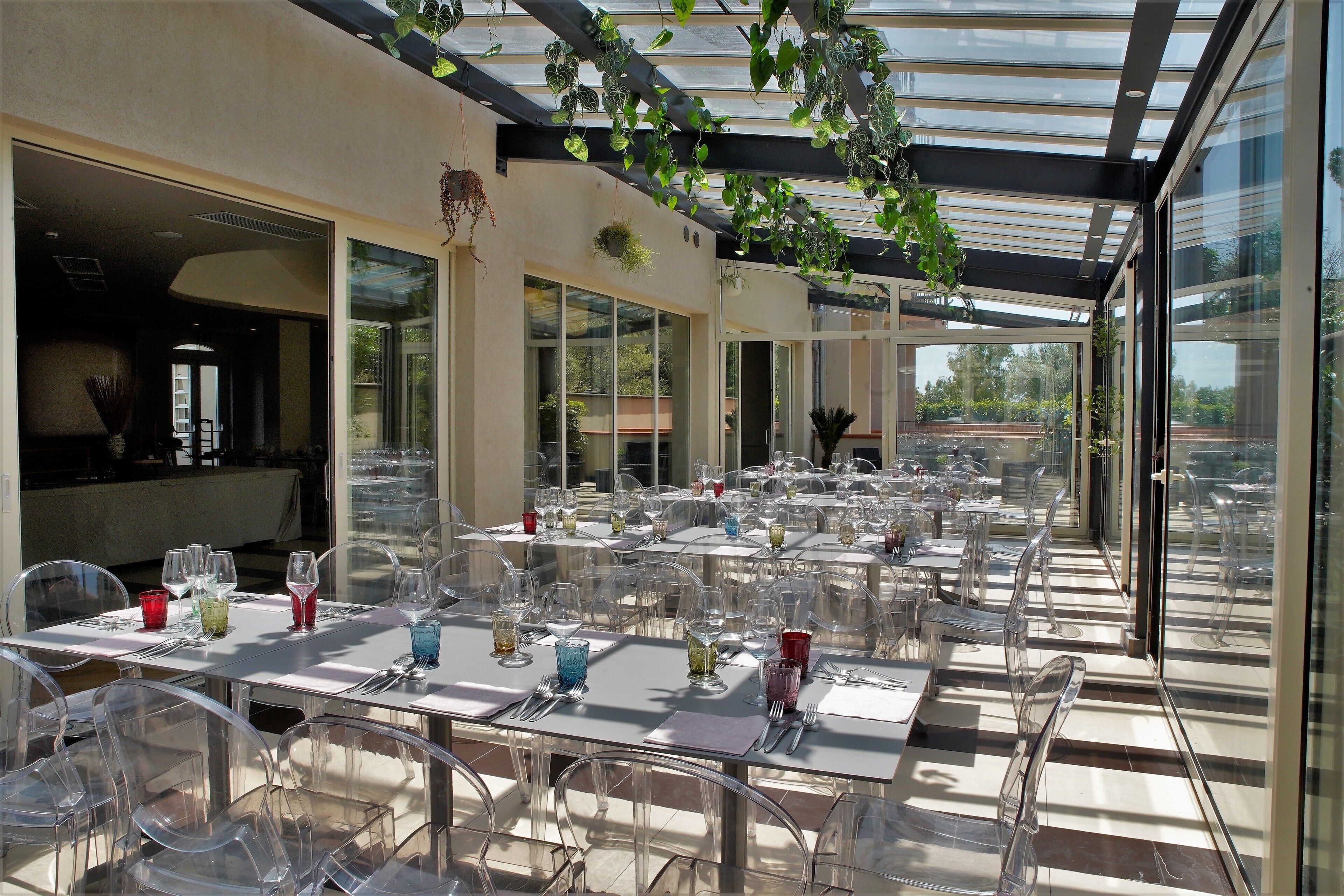 Un restaurant doté d’une terrasse, de tables et de chaises en verre transparent, et d’un plafond en verre orné de plantes.