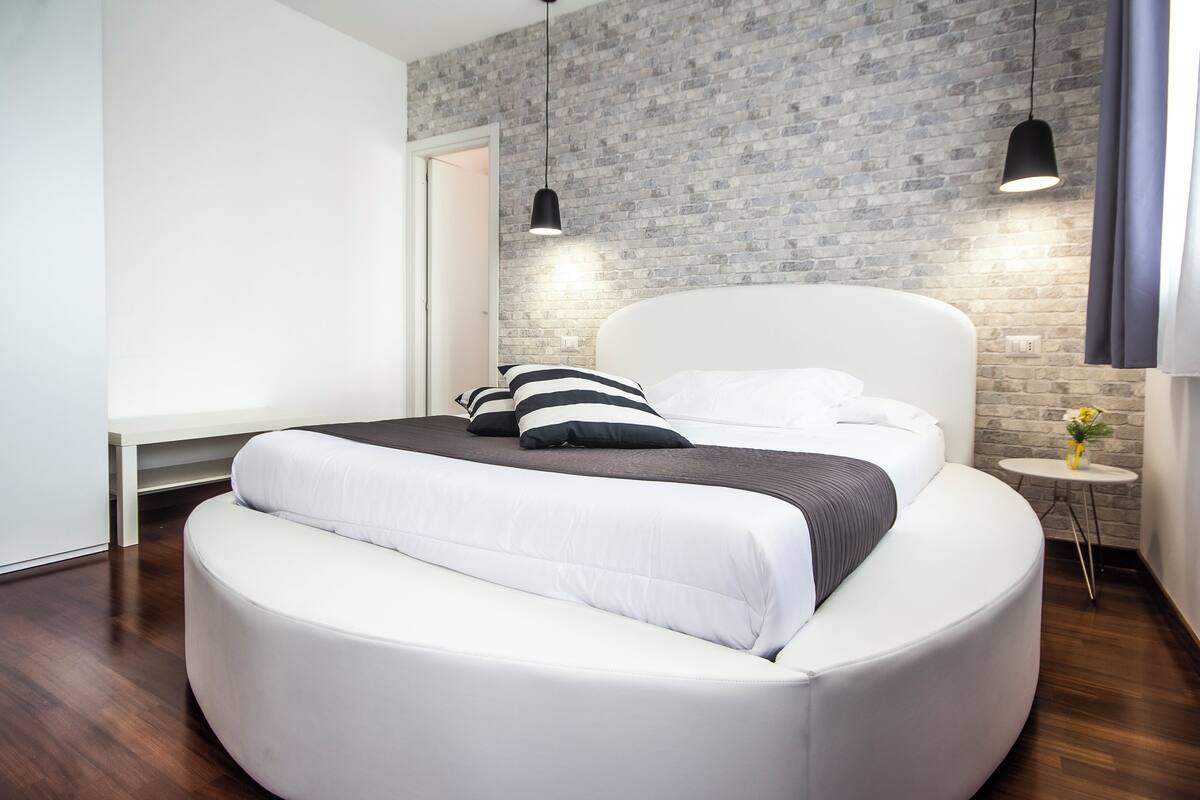 A modern bedroom with a curved bed, a brick-patterned wall, and pendant lighting.
