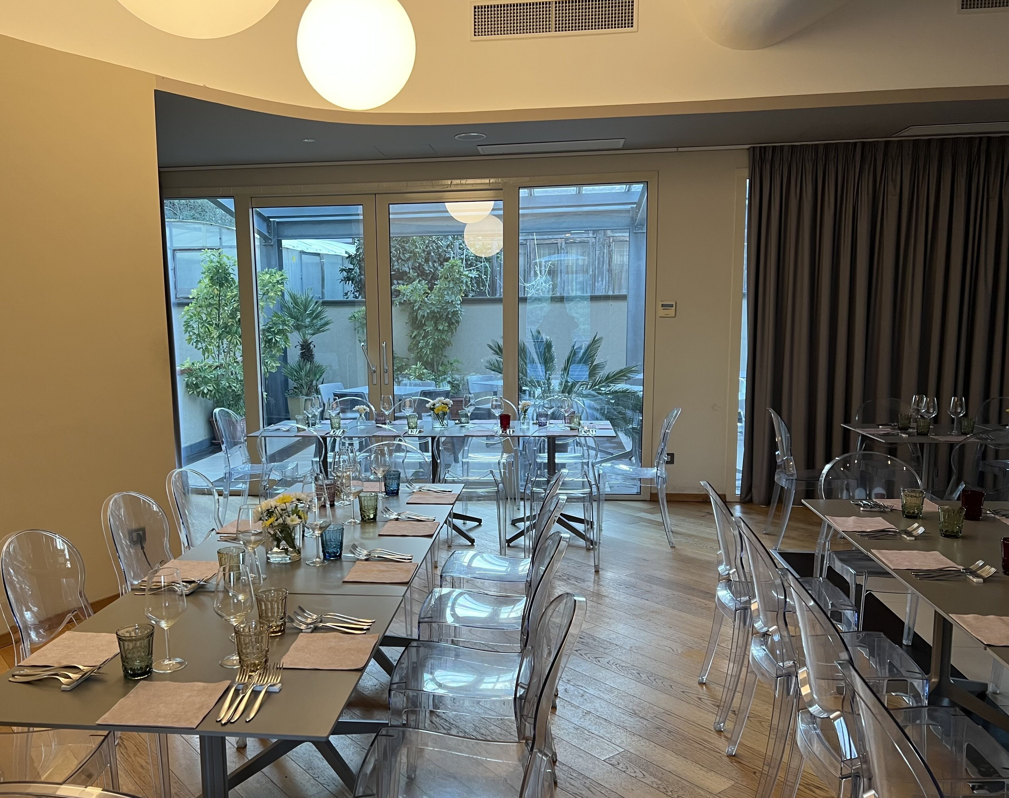 A dining area with clear glass tables and chairs, large windows offering a view of the outdoors, and a modern ceiling design.