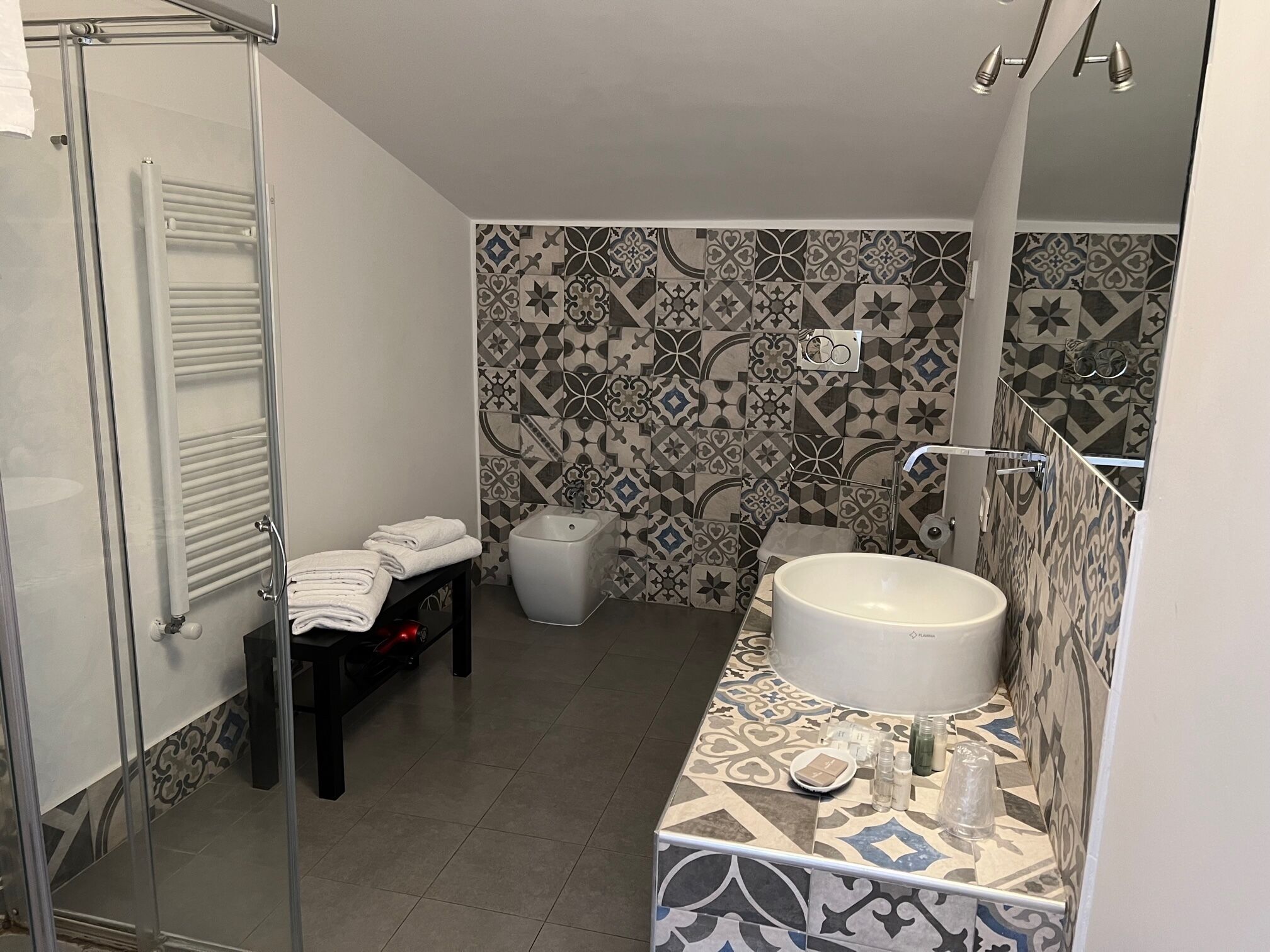 A bathroom with a glass shower enclosure, a white sink, and patterned tiles.