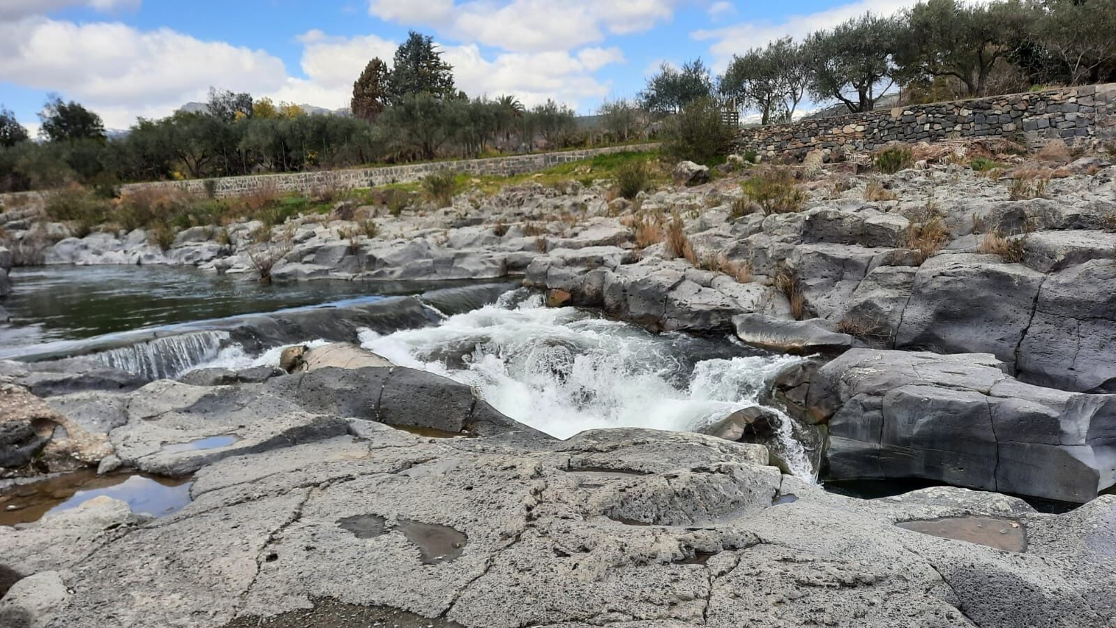 A rocky landscape with a small waterfall and a stone wall in the background.