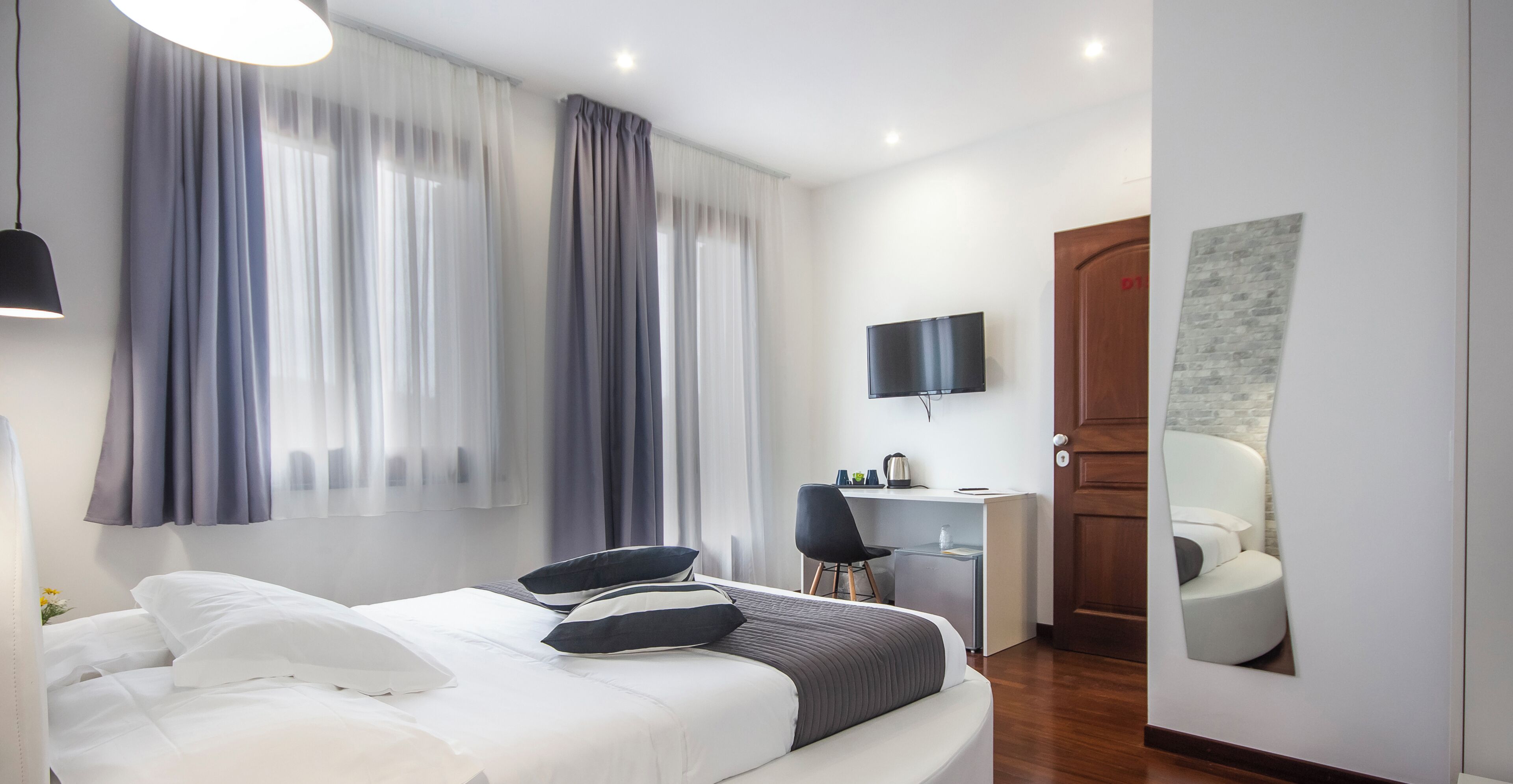 Una habitación de hotel moderna con cama, escritorio, silla, televisor y puerta.