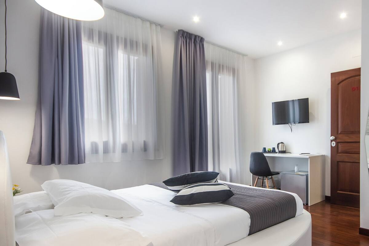 A modern hotel room with a bed, a desk, a chair, a TV, and a door.