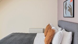 Un dormitorio con cama, almohadas, un radiador y una obra de arte en la pared.