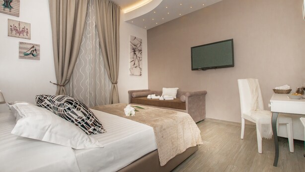 A modern hotel room with a bed, a sofa, a TV, and a dining area. - Elenoire Rooms & Suite (Rome)