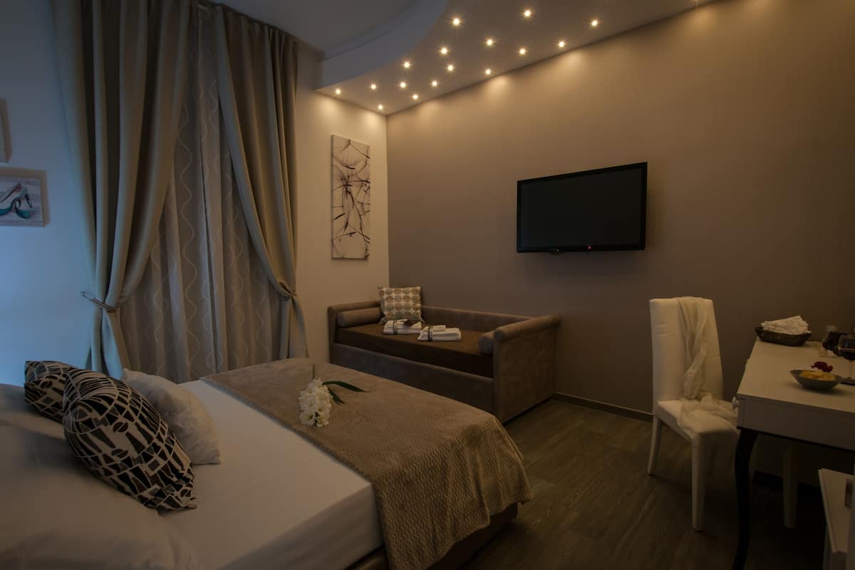 A hotel room with a bed, a sofa, a TV, a dining table, and a chair.