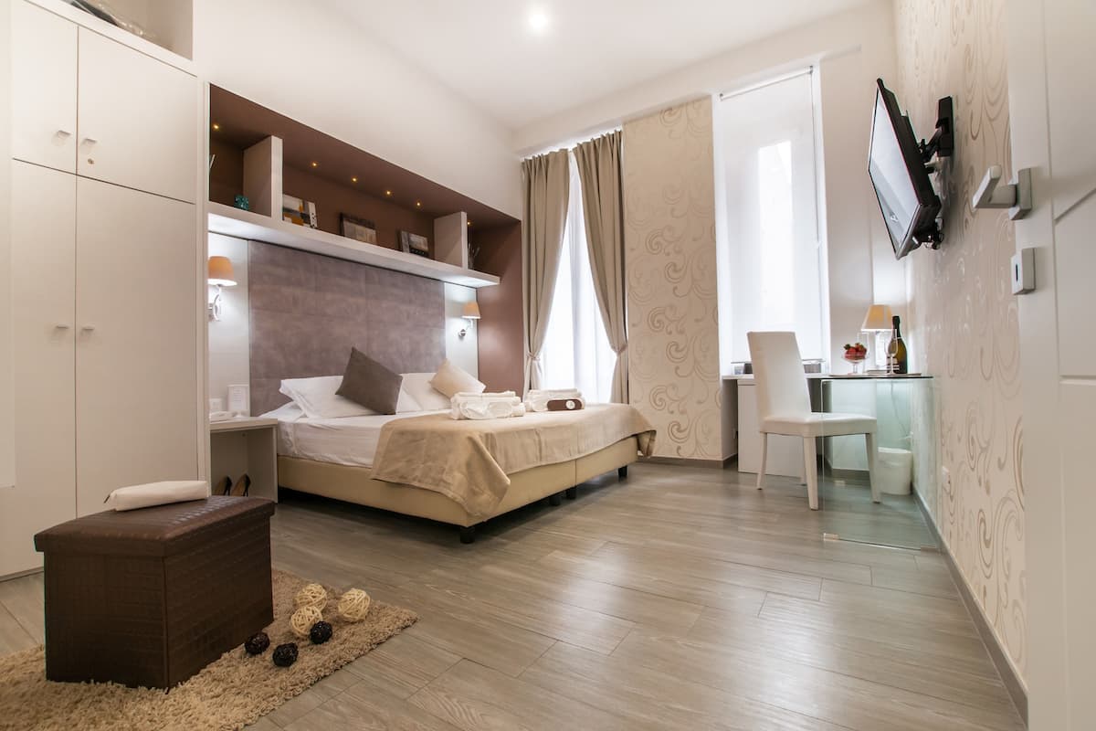 A modern bedroom with a bed, bedside tables, a TV mounted on the wall, and a small desk area.