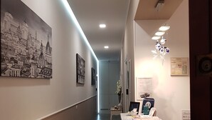 A hallway with a long wooden floor, a desk with a computer and papers, and a wall with framed pictures. - Elenoire Rooms & Suite (Rome)