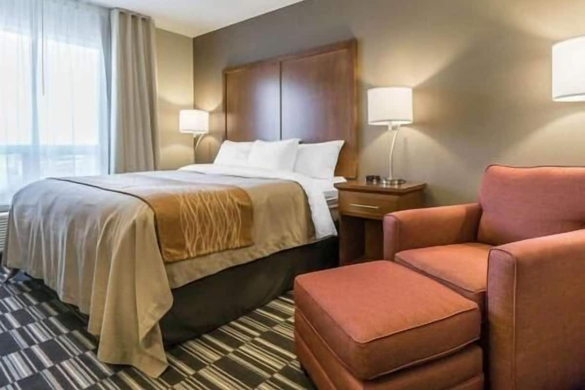 A hotel room with a bed, two bedside tables with lamps, a chair, and a patterned carpet.