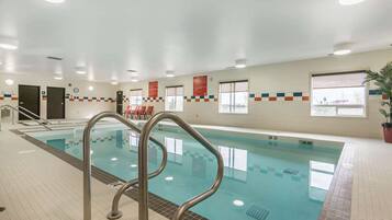 An indoor swimming pool with clear lane markings, metal pool ladders, and tiled walls with informational posters.