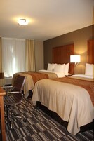 Una habitación de hotel con dos camas, un escritorio, una silla y una lámpara.