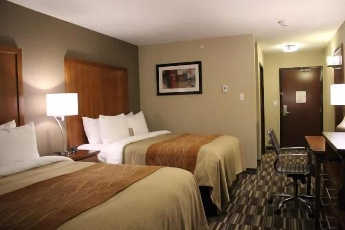 A hotel room with two beds, a desk, a chair, and a door.