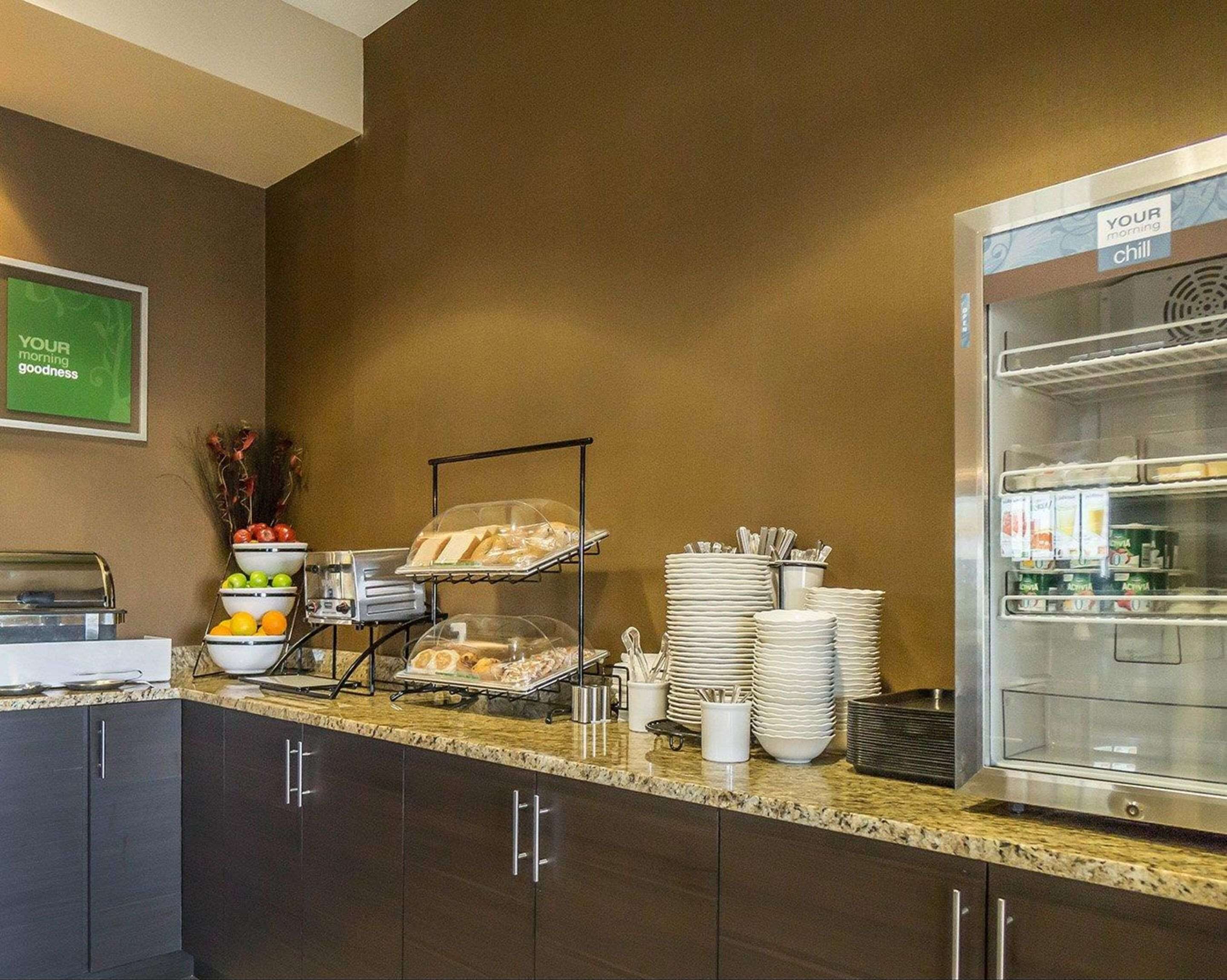 A breakfast buffet setup with various food items, a refrigerator, and a sign saying "YOUR morning goodness".