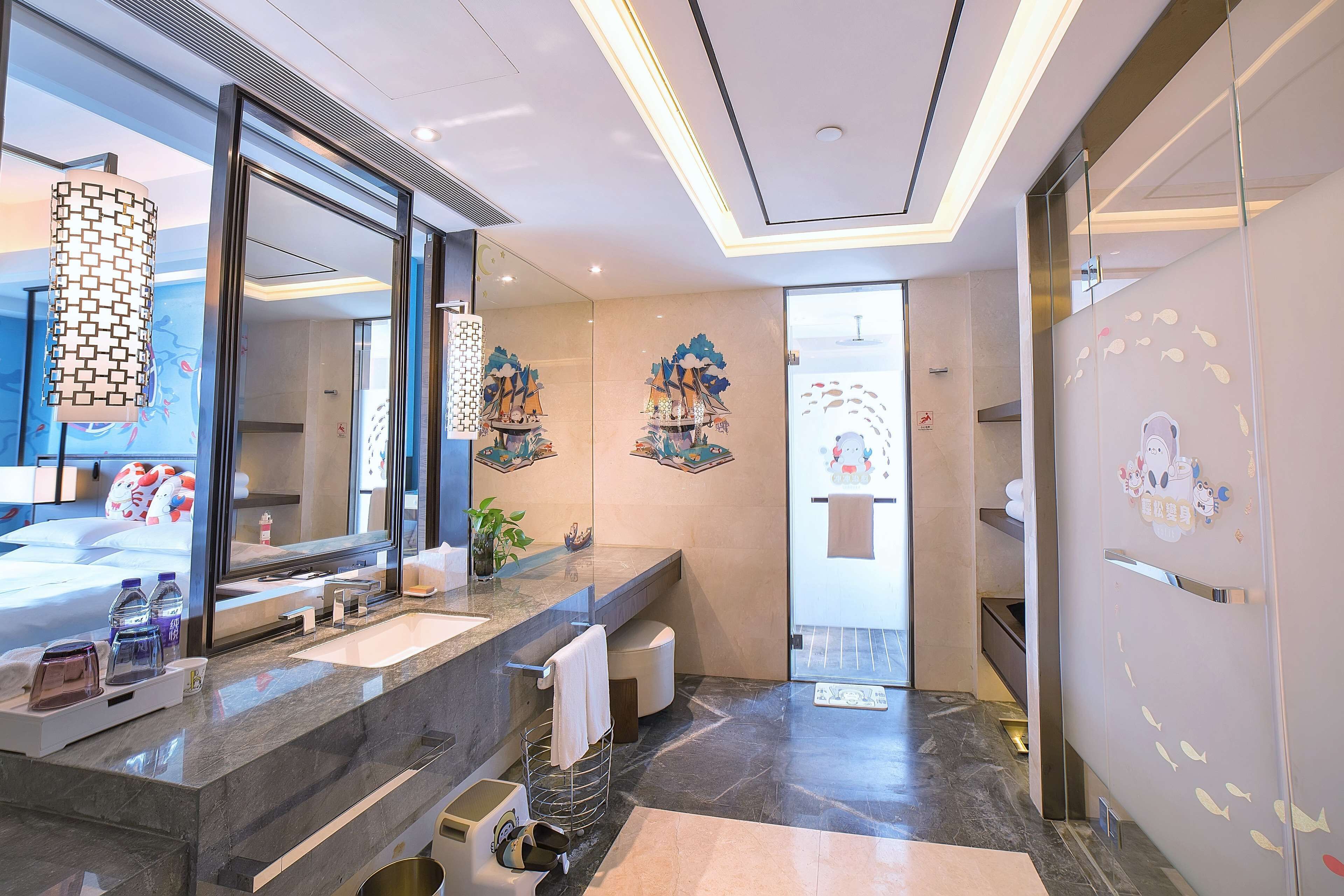 A modern bathroom with a large mirror, a sink, and a toilet. There are decorative wall art pieces and a towel rack.