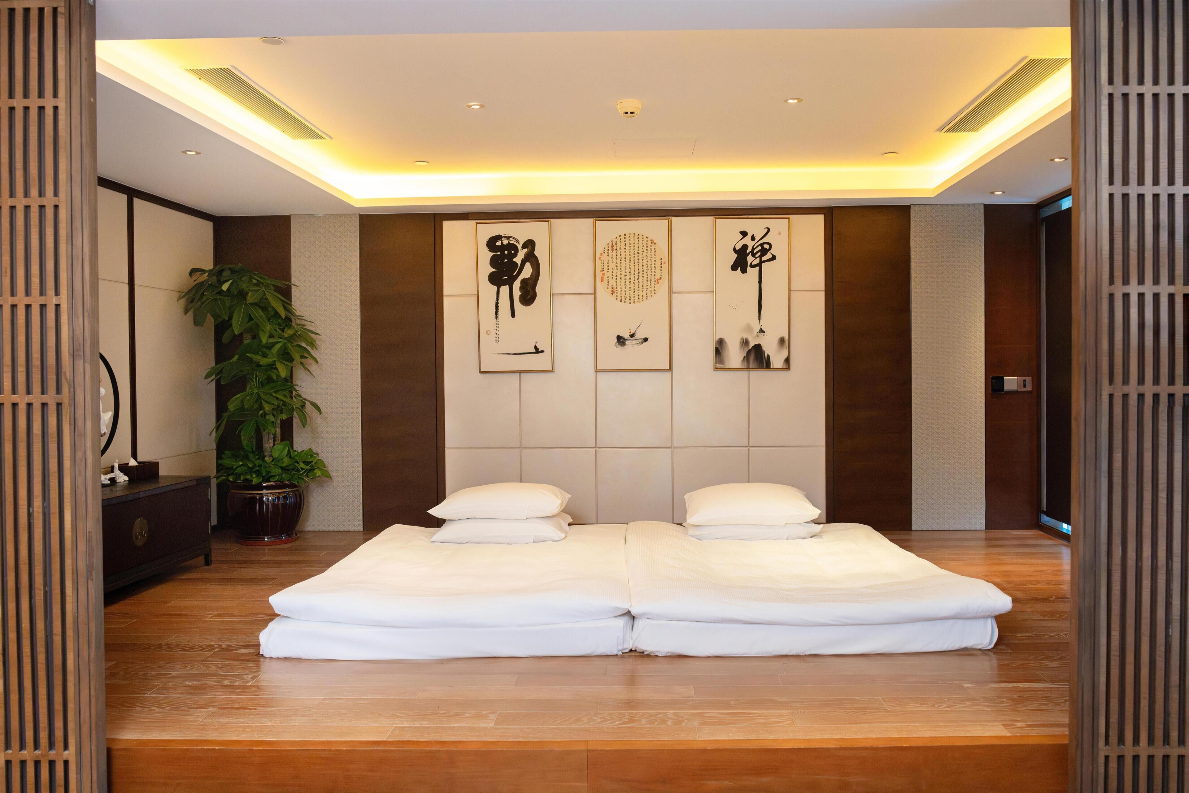 A modern bedroom with a large bed, a potted plant, and artwork on the wall.