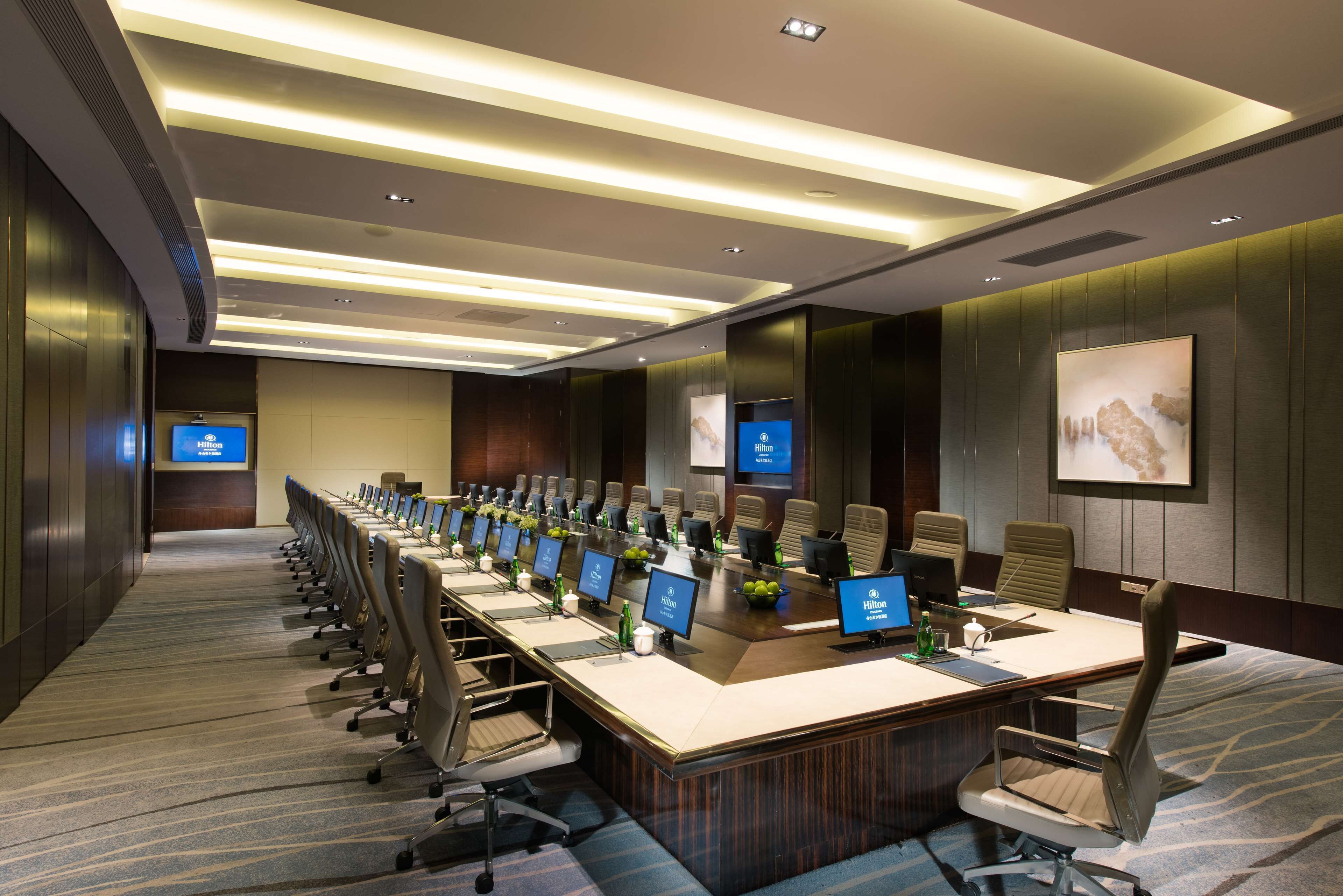 A conference room with a long table, multiple chairs, and several monitors.