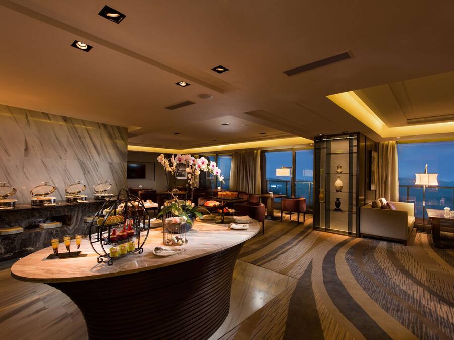 A modern hotel lobby with a marble reception desk, a seating area, and a large window offering a city view.
