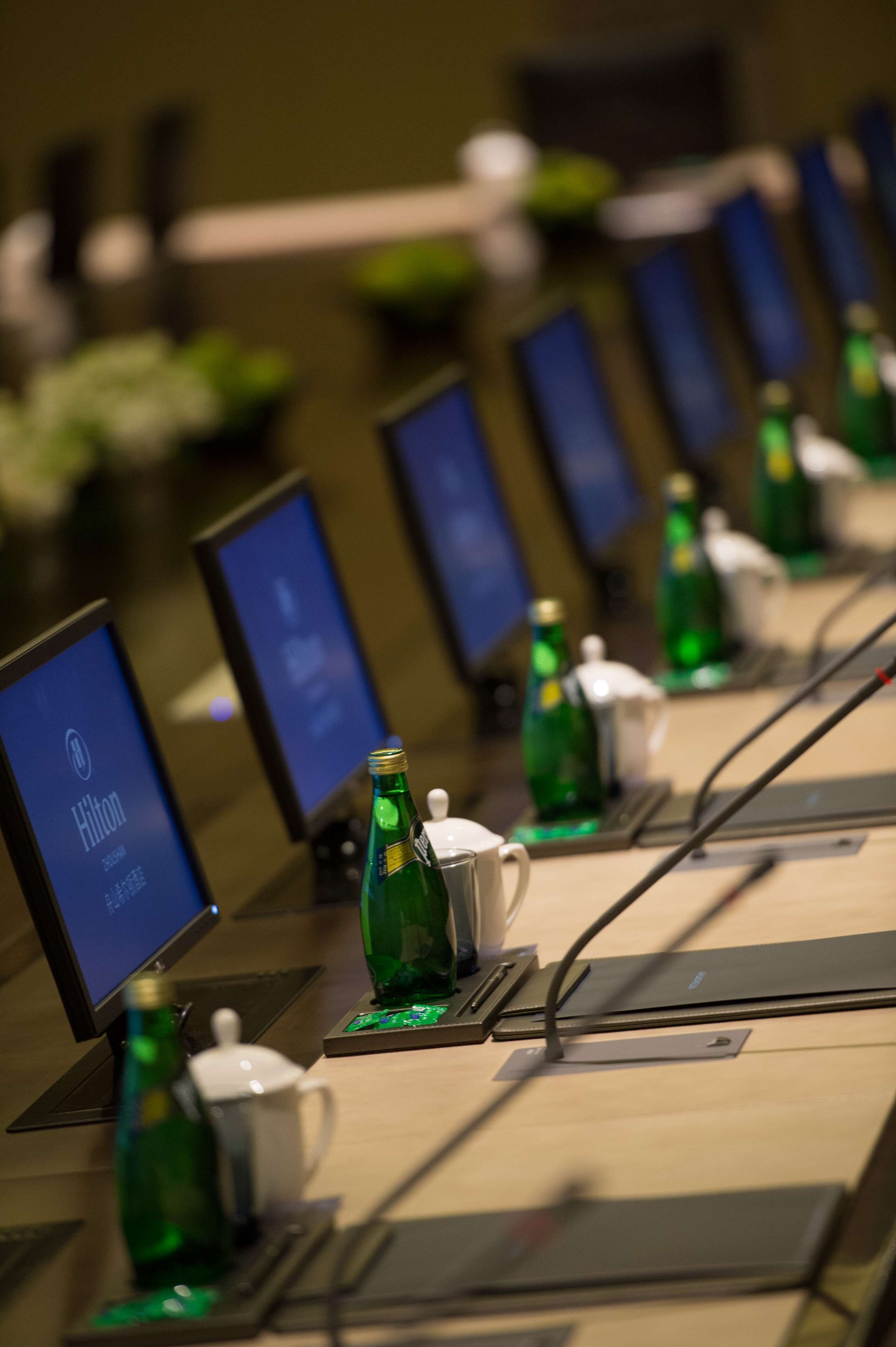 Zona de recepción de un hotel con varios monitores que muestran el logotipo de Hilton, botellas verdes y una taza blanca sobre un mostrador.