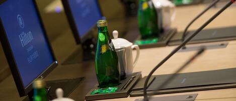 Zona de recepción de un hotel con varios monitores que muestran el logotipo de Hilton, botellas verdes y una taza blanca sobre un mostrador.