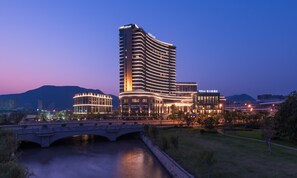 A modern hotel with a curved facade, a bridge, and a river in the foreground. - Hilton Zhoushan (Zhoushan)