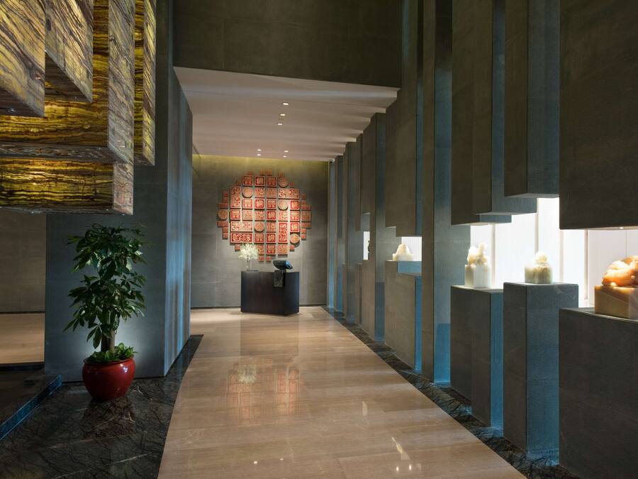 Um lobby moderno com piso de mármore polido, balcão de recepção, uma grande parede decorativa e uma planta em vaso.