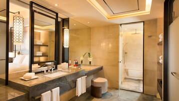 Un baño moderno con un espejo grande, encimera de mármol, un taburete redondo y una zona de ducha separada.