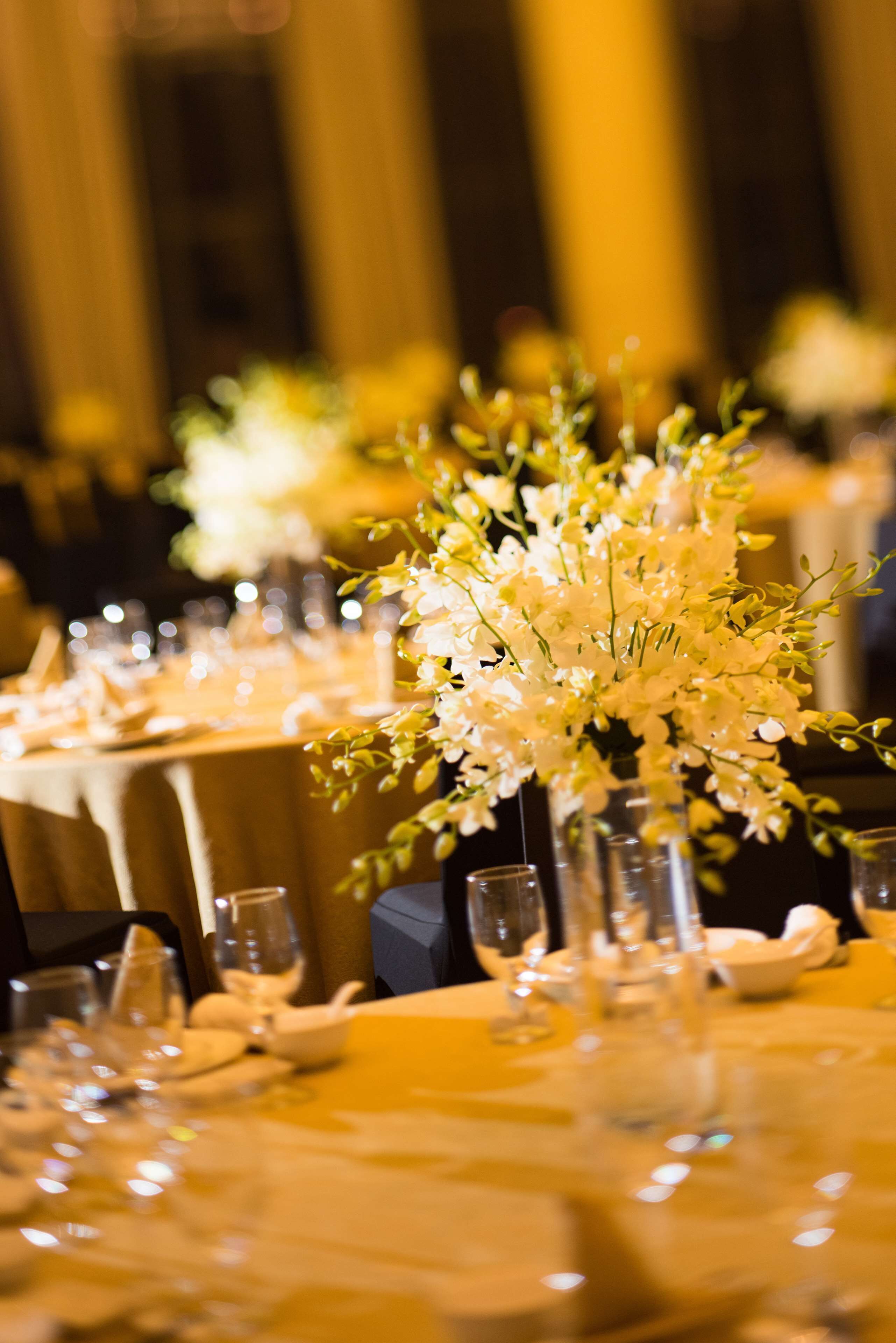 Une salle de banquet où les tables sont dressées pour un événement formel, avec des compositions florales et de la verrerie transparente.
