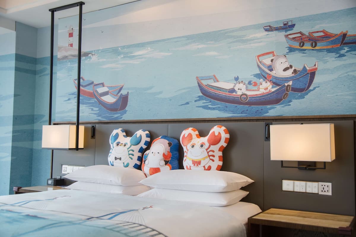 A hotel room with a large bed, two bedside lamps, a nightstand, and a wall-mounted TV.