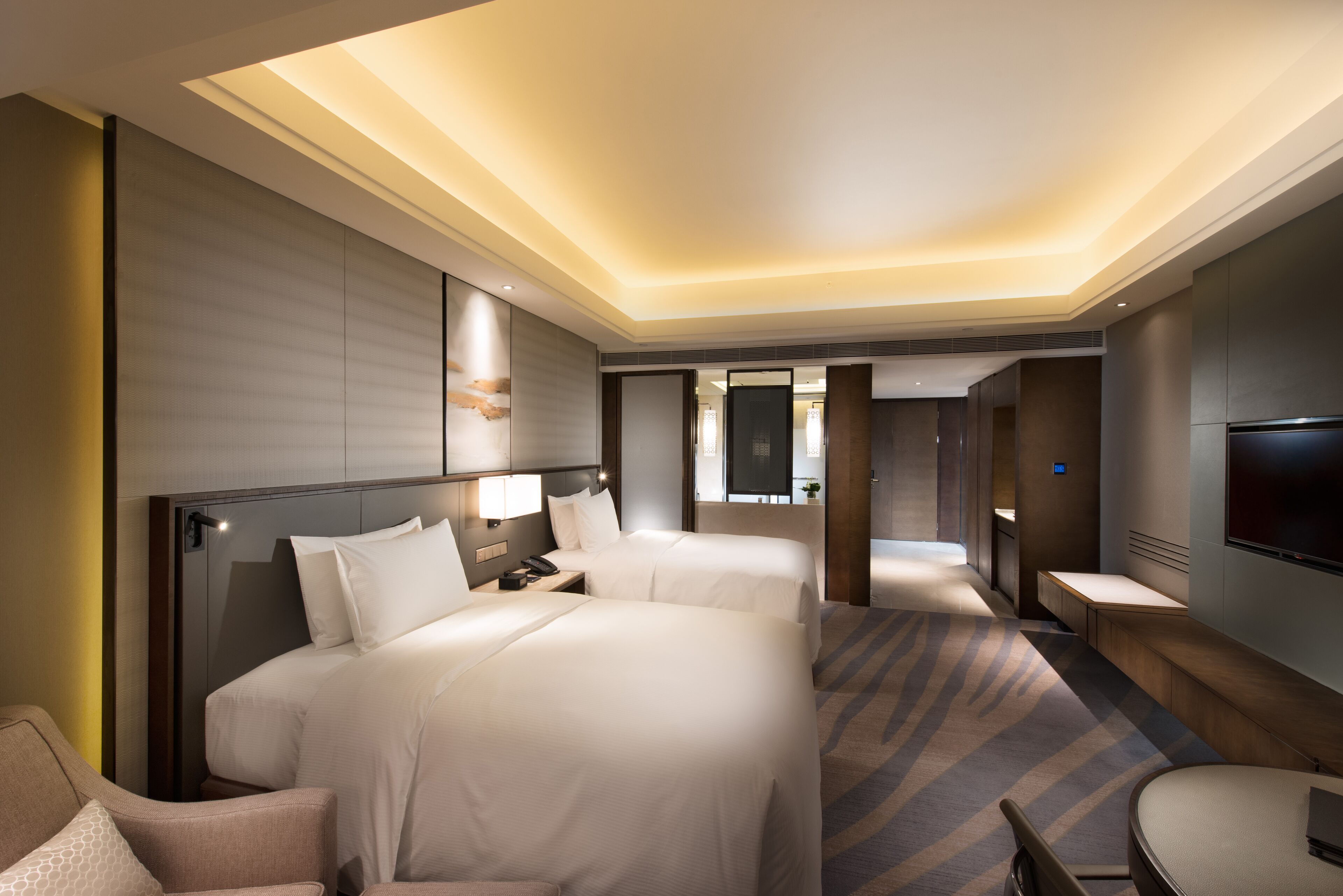 A hotel room with two beds, a desk, a chair, a TV, and a large mirror.