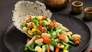 Un plato negro con una variedad de verduras y frutos secos, acompañado de un encaje blanco y una maceta marrón al fondo.