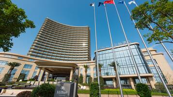 Un hotel moderno con fachada curva, varios mástiles de bandera y un jardín cuidado.