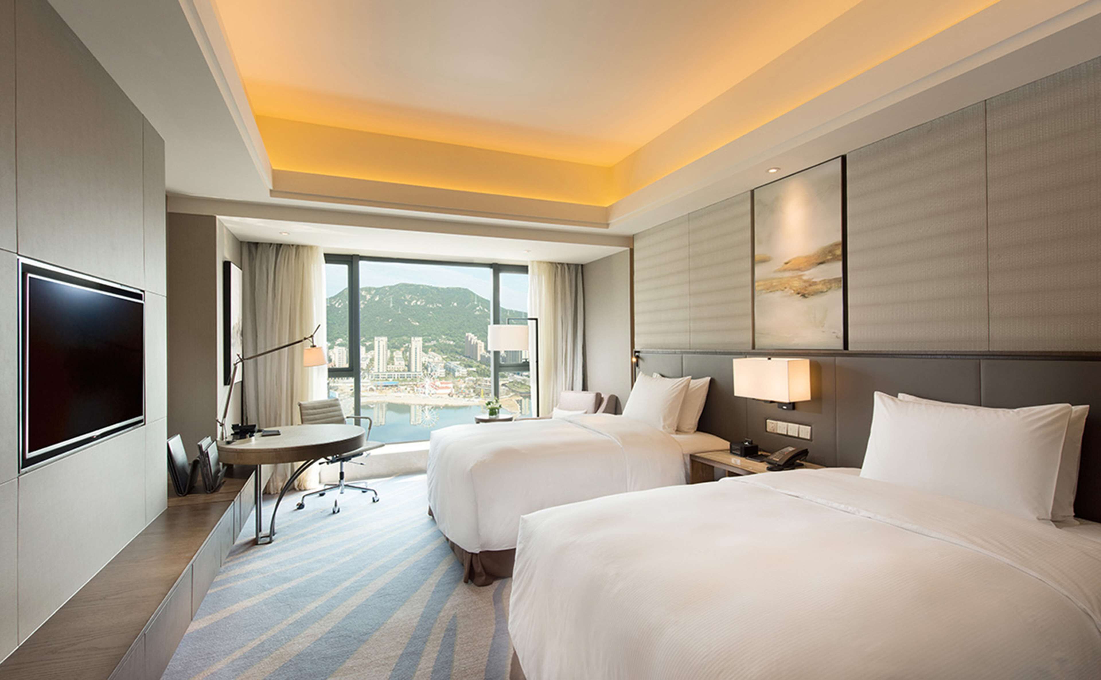 Habitación de hotel con dos camas, un escritorio, televisión y un ventanal con vista a la ciudad.